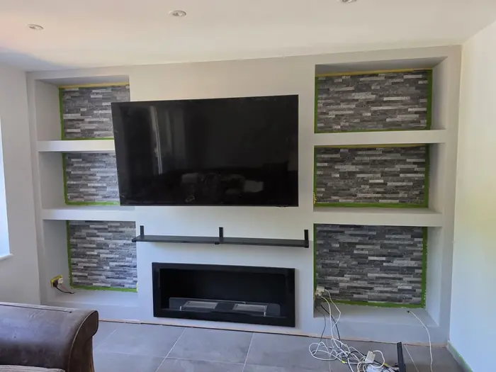 The finished media wall with stone-clad recesses, concealed lighting and a fire
